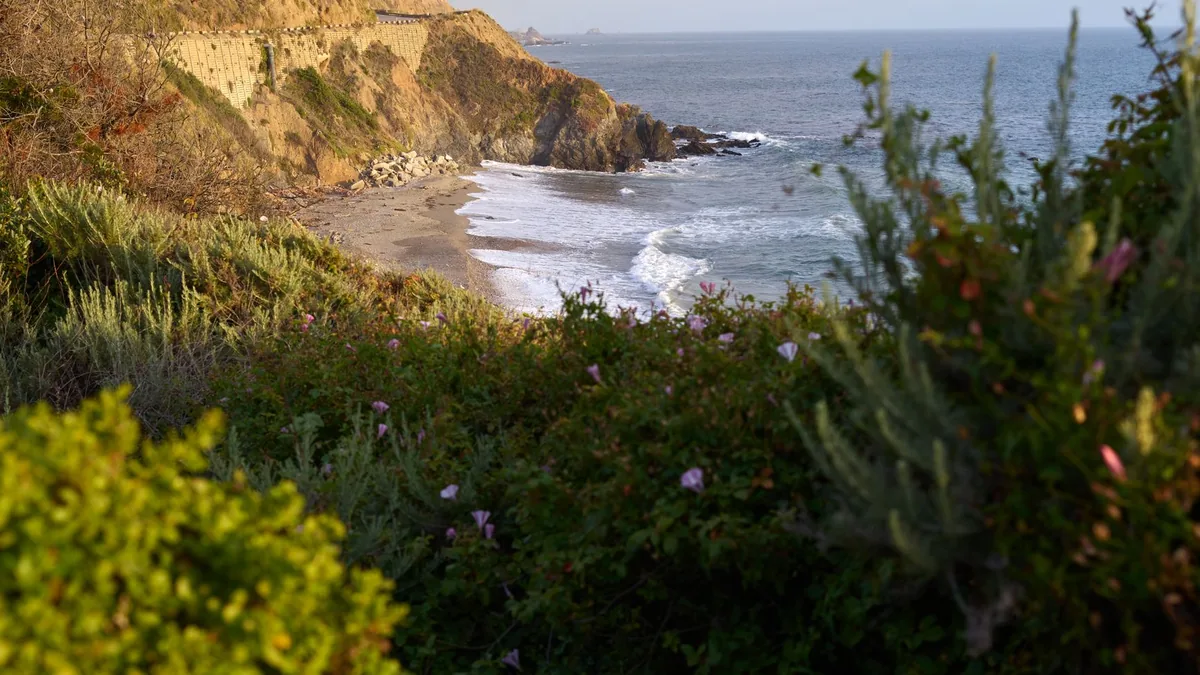 Beautiful coastal landscape featuring waves, cliffs, and lush greenery.